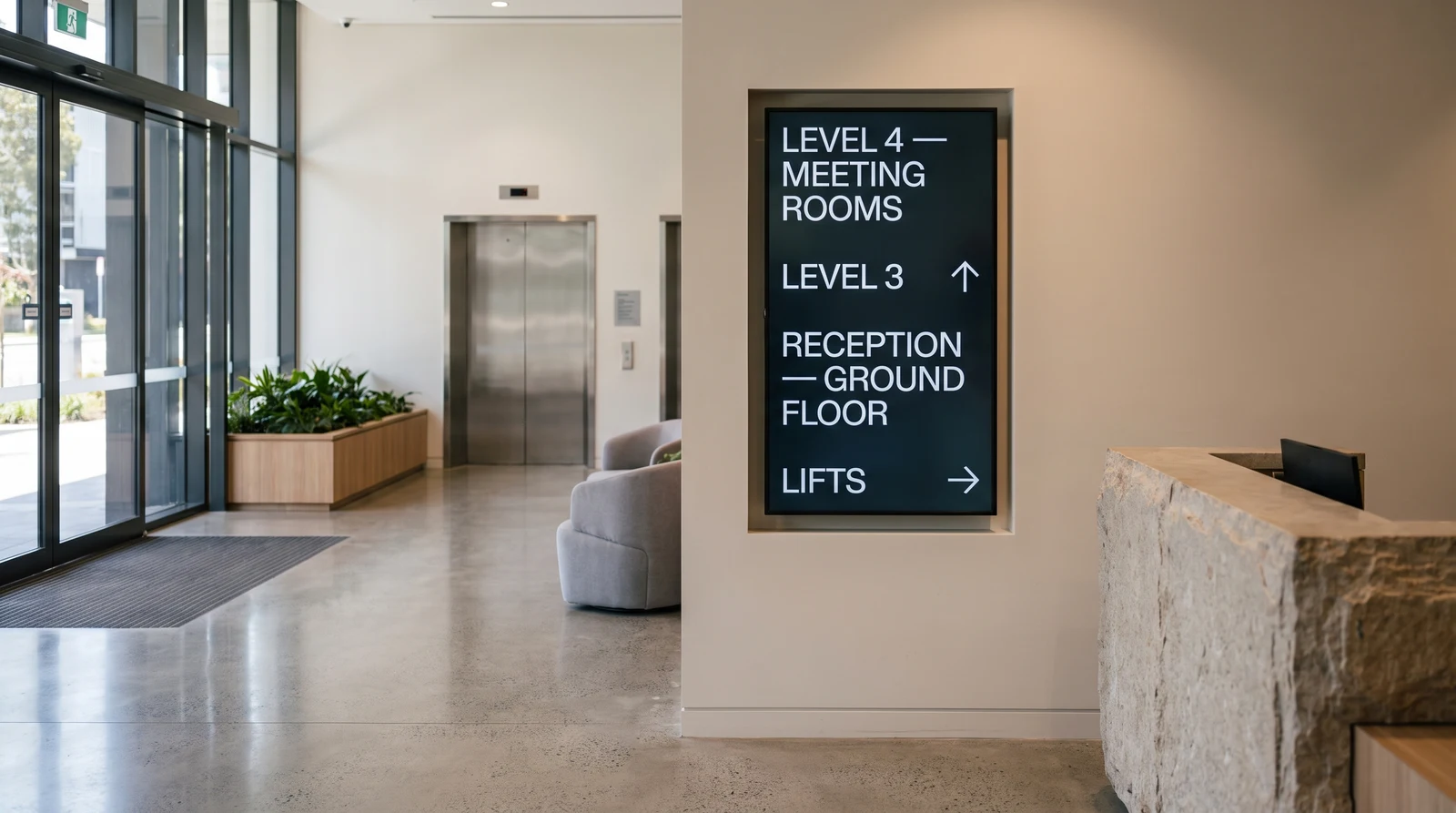 Portrait digital directory board listing floors and lifts on the wall of a commercial office building lobby beside the reception desk