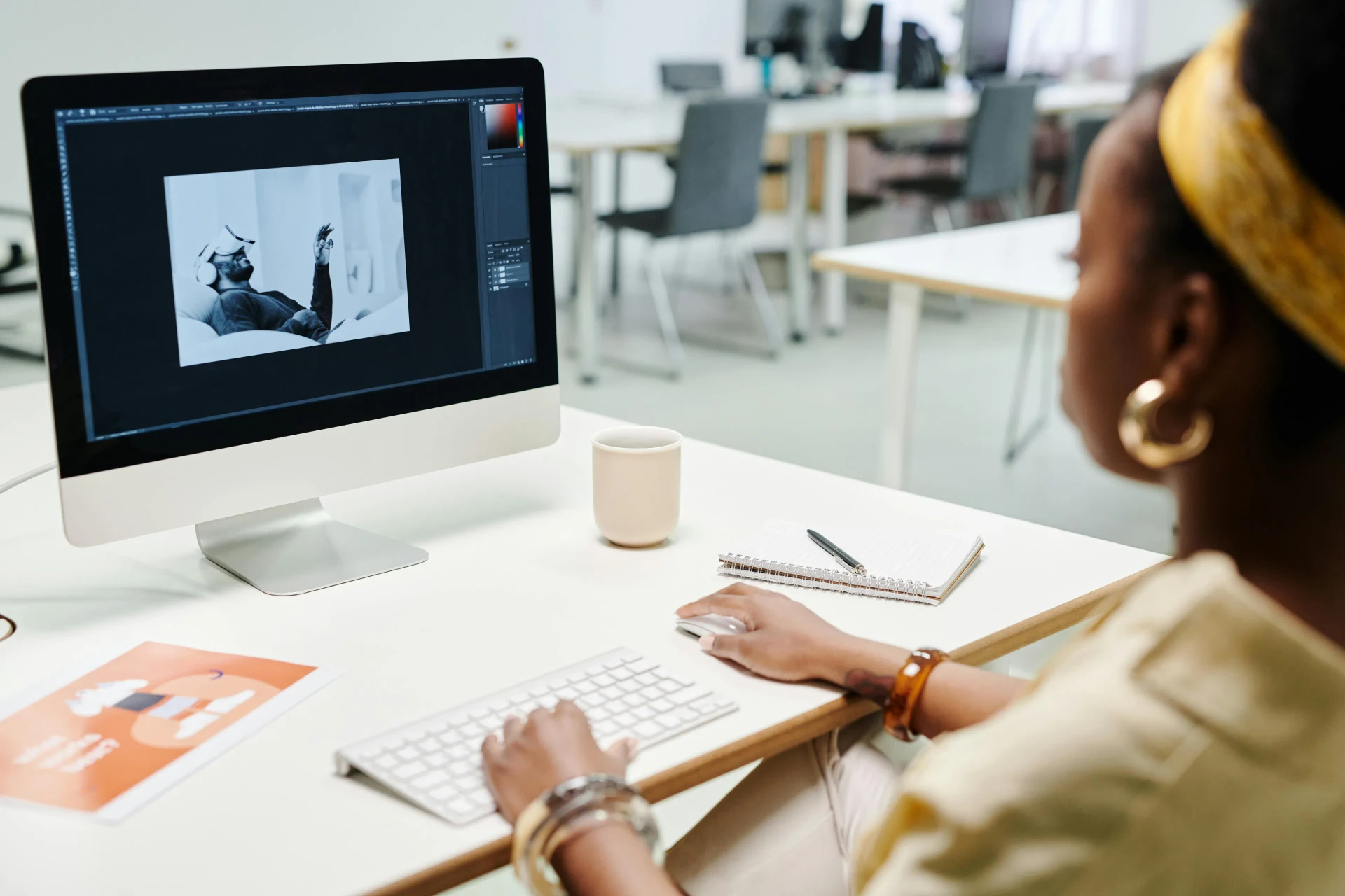 Graphic designer editing a promotional poster in Photoshop on a desktop screen at a studio desk
