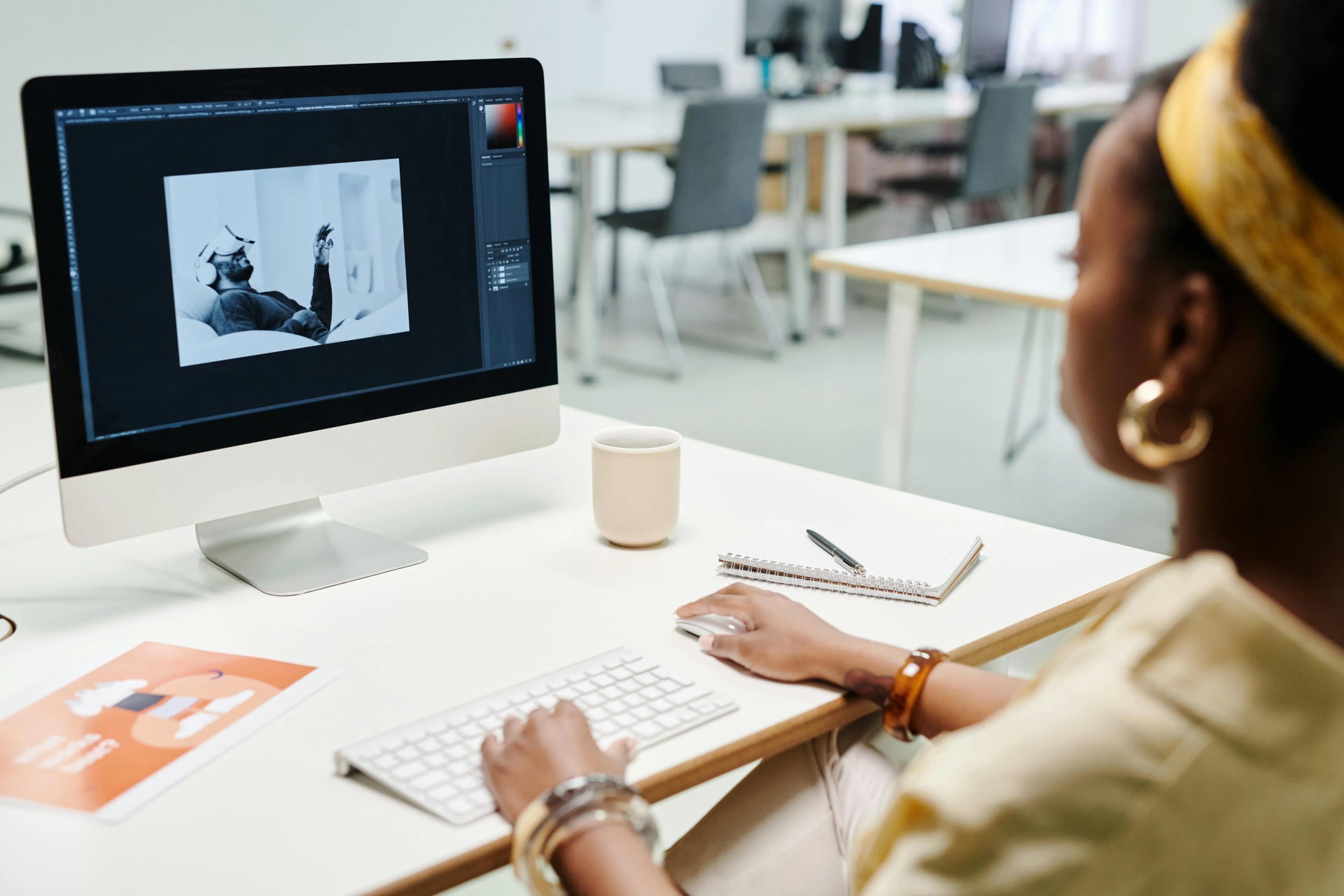Graphic designer editing a promotional poster in Photoshop on a desktop screen at a studio desk