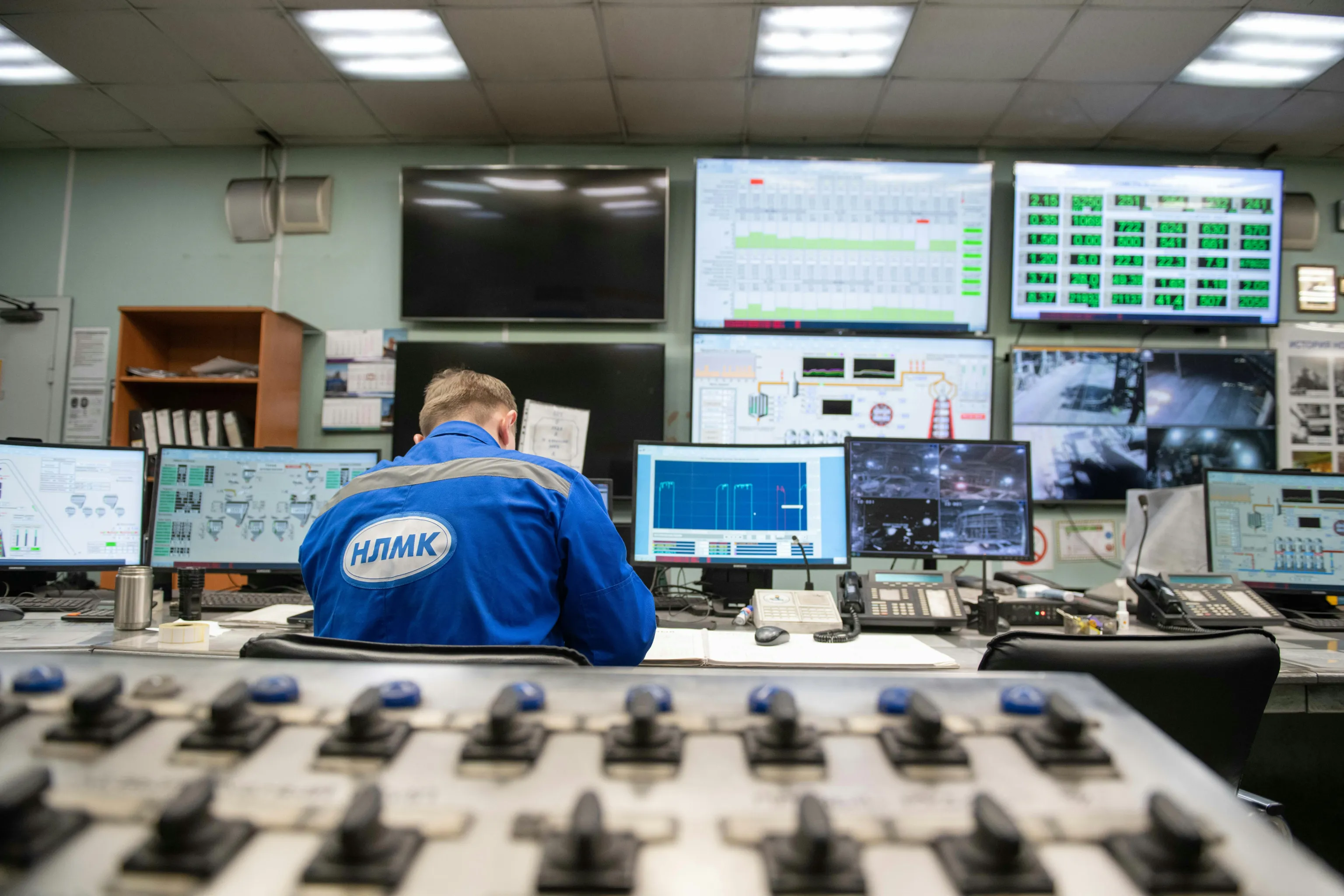 Operator at an industrial control room desk surrounded by screens showing plant monitoring dashboards