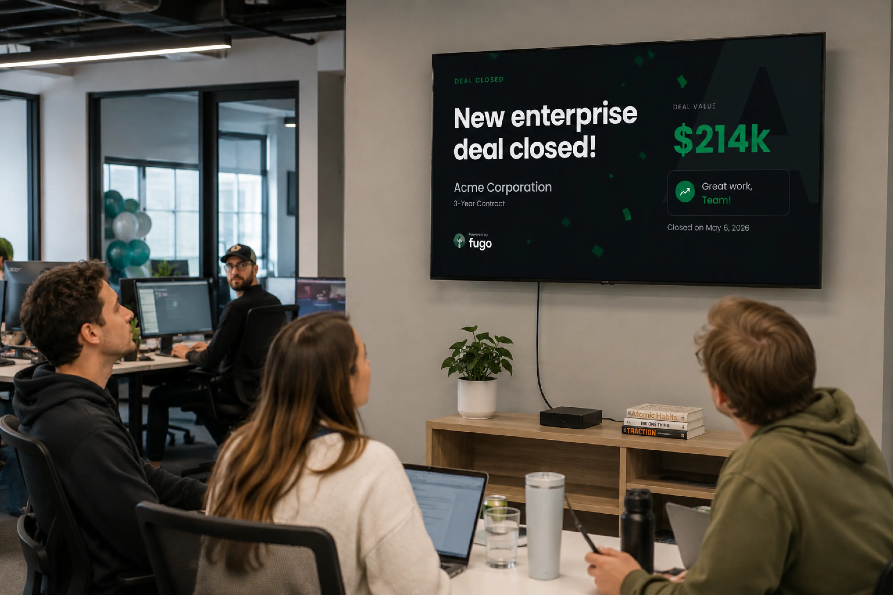 Sales team gathered around an office TV displaying a new enterprise deal-closed celebration triggered from the CRM