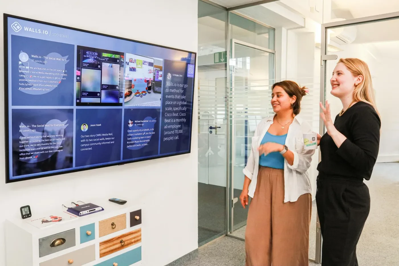 Two people viewing a wall-mounted social media wall in a modern open space