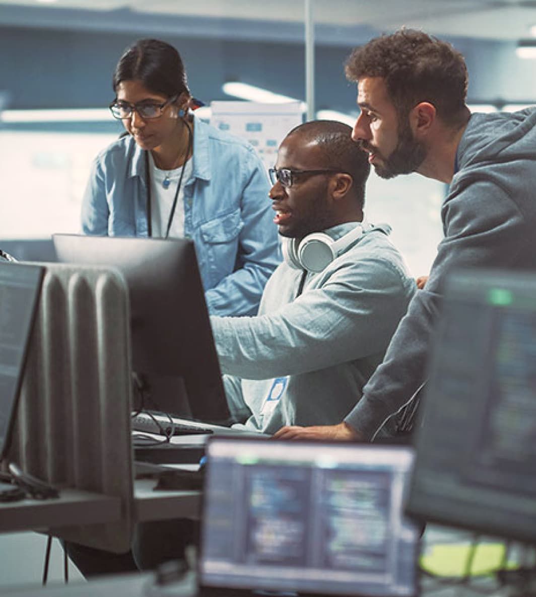 An IT team is gathered around a computer in an office. They are looking at the monitor. UI elements of Fugo's digital signage software are overlain on the photo.