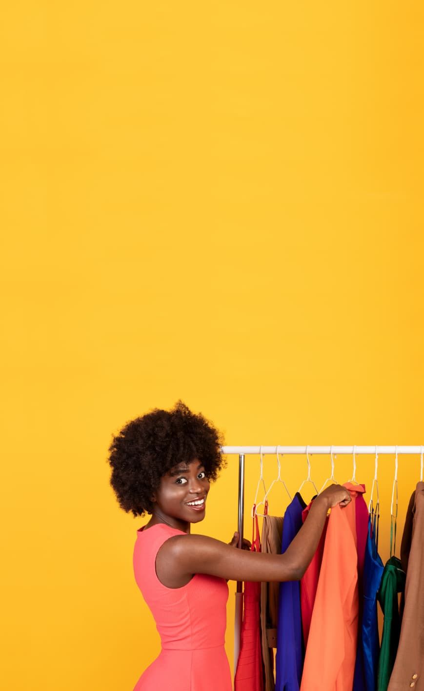 A woman stands in front of a clothing rack in a retail shop and smiles.