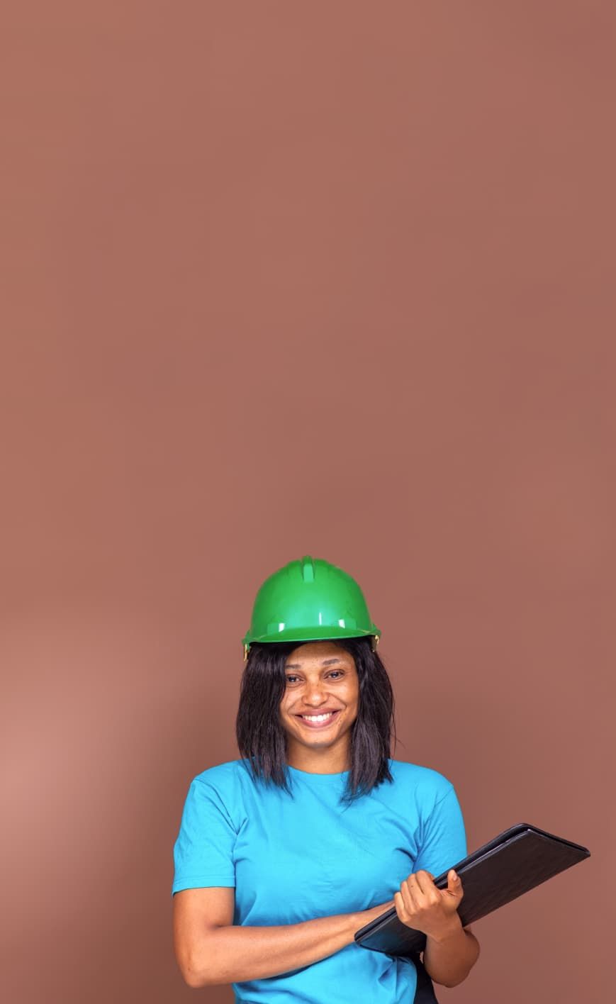 A woman wearing a hard hat stands in front of a wall.