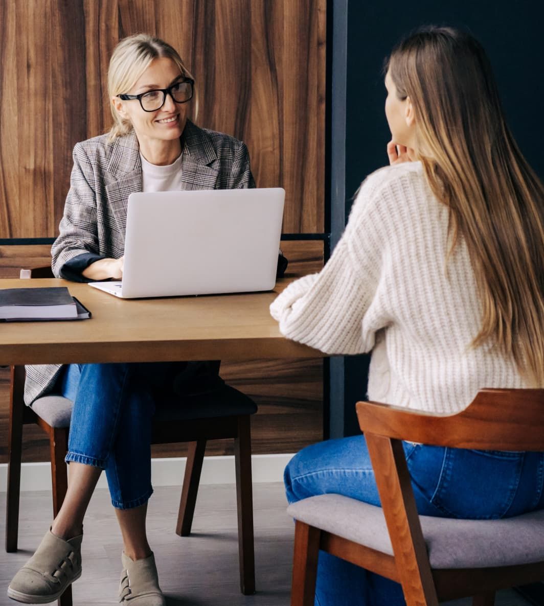 Two women are sitting across from each other at a table in an office, having a meeting. UI elements of Fugo's digital signage solution are overlain on the photo.