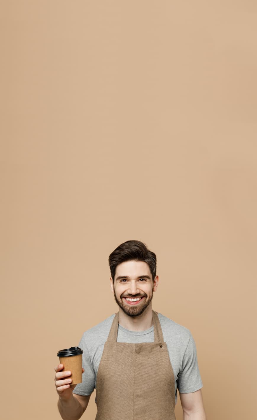 A barista holds a coffee in front of a cafe wall and smiles at the reader.